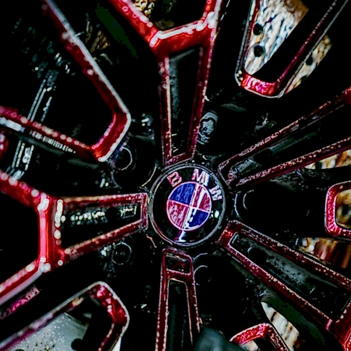 Un gros plan sur une jante de voiture affiche un logo BMW au design noir et rouge épuré. Les gouttes deau sur la surface brillante et humide soulignent lefficacité du nettoyant pour jantes et déferrifiant Nanolex. - Tekalab